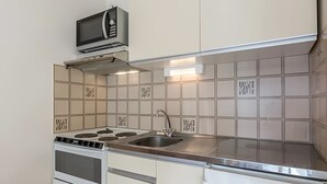 Een kleine keuken met een magnetron, fornuis, spoelbak en witte kastjes.