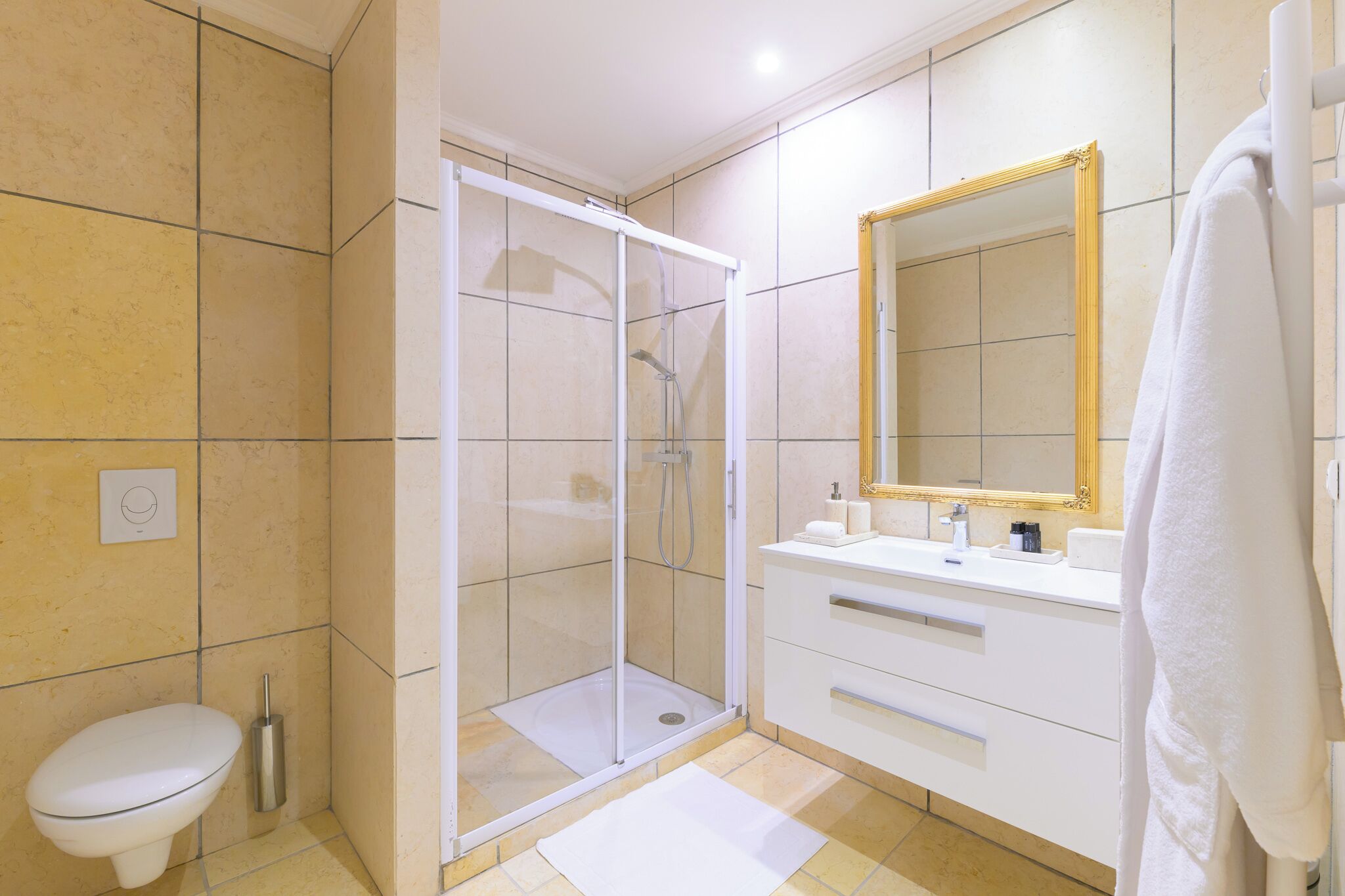 Een moderne badkamer met een glazen douchecabine, een wit toilet, een wastafel met spiegel en een handdoek aan de muur.