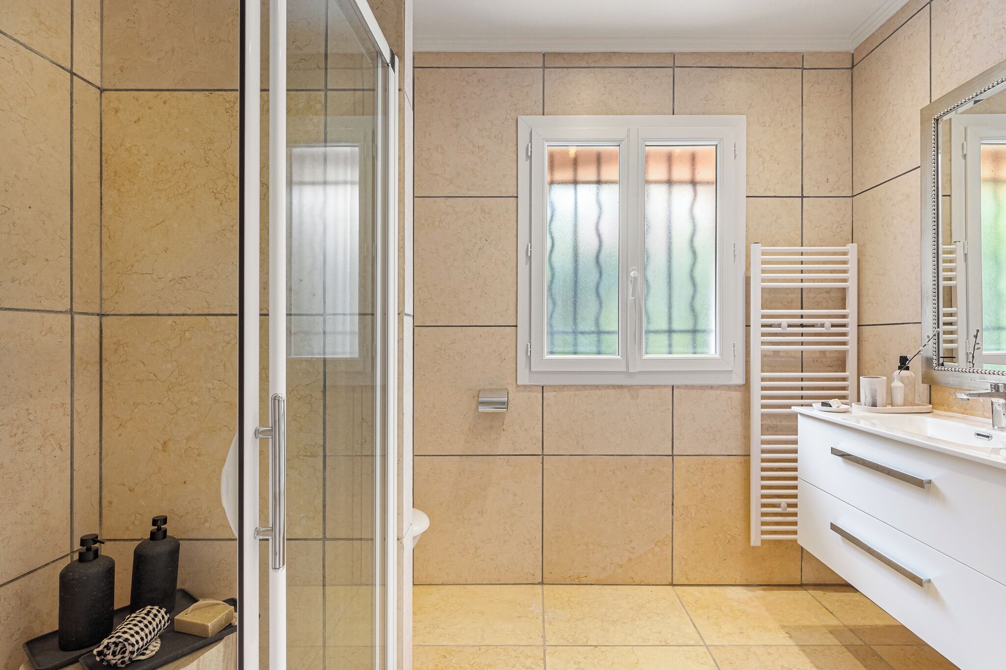 Une salle de bain moderne avec une douche à parois de verre, un meuble-lavabo blanc doté d’un miroir et une fenêtre à verre dépoli.