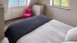 Un dormitorio con cama, una silla rosa, un ventanal con vistas al mar y un radiador.