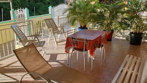 A balcony with outdoor seating, including chairs and a table, surrounded by potted plants. - Detached house rated 03 stars, comfortable, equipped, with Wifi (deshaies)