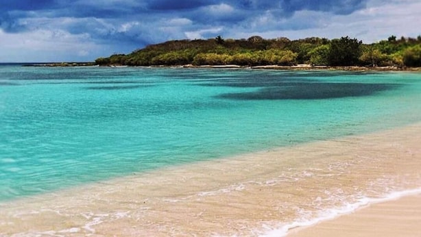 A beach with clear turquoise water, sandy shore, and a distant island under a cloudy sky. - Detached house rated 03 stars, comfortable, equipped, with Wifi (deshaies)