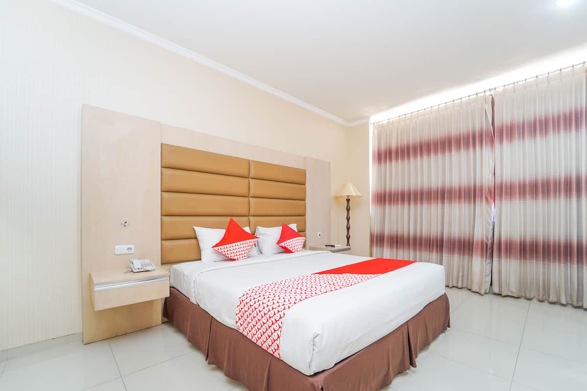 A hotel room with a large bed, a nightstand with a phone, a lamp, and a window with curtains.