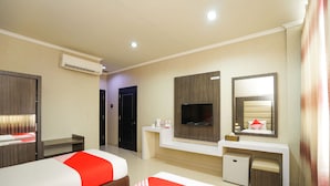 Quarto de hotel com duas camas, televisão, escrivaninha, espelho e ar condicionado.