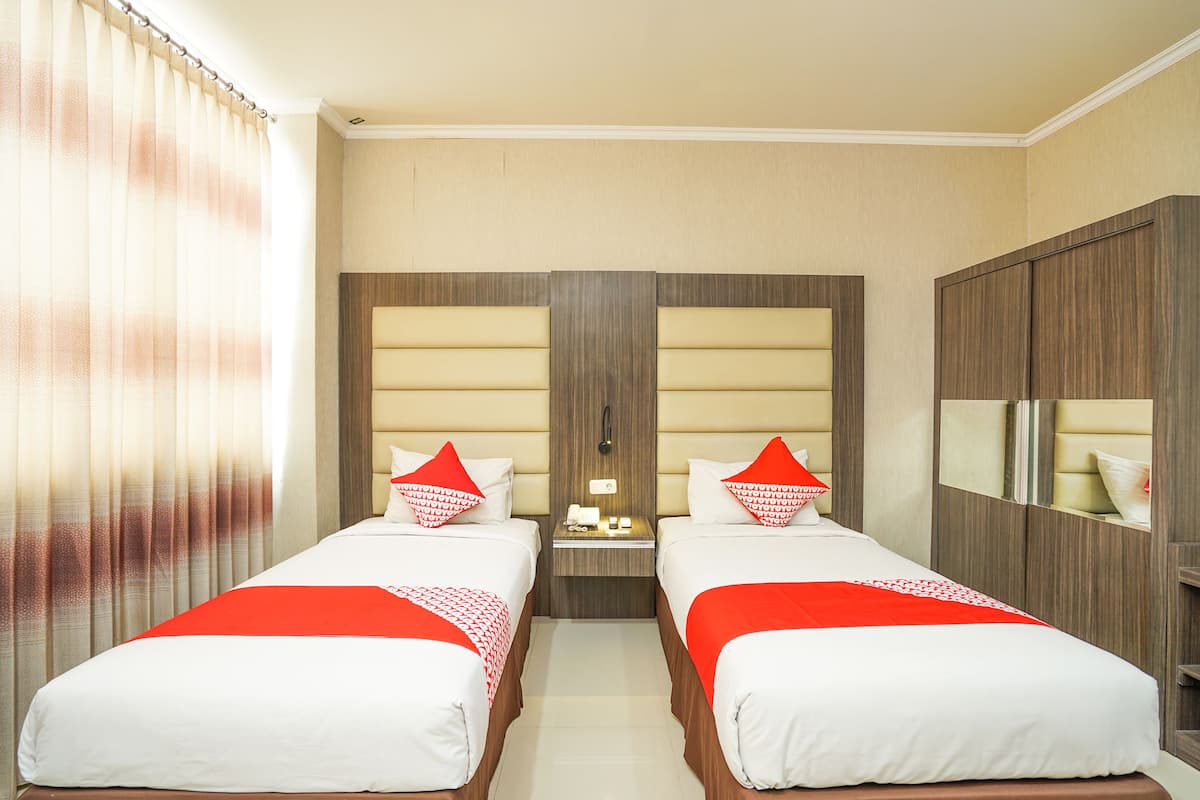 A hotel room with two beds, a nightstand, a mirror, and a wardrobe.