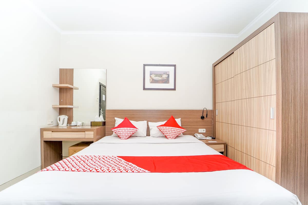 A hotel room with a bed, a wooden wardrobe, a bedside table, a mirror, and a framed picture on the wall.