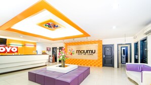 Uma área de recepção de hotel com balcão, espaço de estar com sofás roxos e uma parede com o nome do hotel 'maumu hotel and lounge'.
