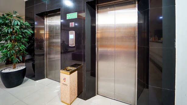 Um elevador com sinalização de saída verde, aviso de proibido fumar e um painel digital.