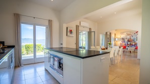 A modern kitchen with a large island, sliding glass doors leading to a balcony, and a dining area with a view. - Magnificent villa at the gates of Saint-Tropez (Gassin)