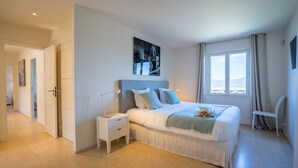 A bedroom with a large bed, bedside tables, a nightstand, a window with curtains, and a painting on the wall. - Magnificent villa at the gates of Saint-Tropez (Gassin)