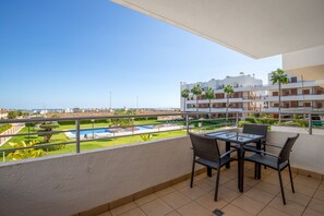 A balcony with a view of a swimming pool and a building with multiple floors and balconies.