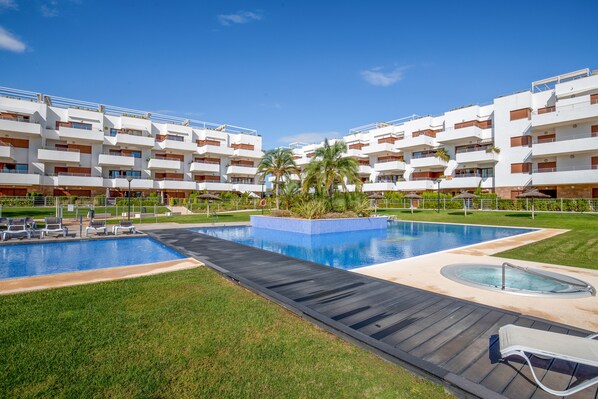 A modern hotel with a swimming pool, sun loungers, and a well-maintained lawn.