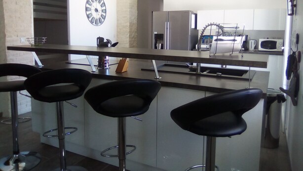 Een moderne keuken met een bar, voorzien van drie zwarte barkrukken. Op de muur is een klok en een bord met de tekst 'CUISINE' te zien.