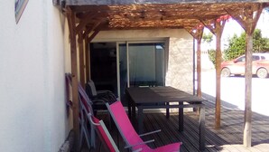 Een terras buiten met een tafel en stoelen, een overdekt gedeelte en uitzicht op een straat met een auto.