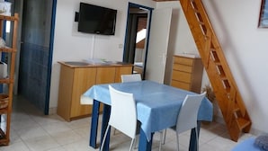 A dining area with a table and chairs, a wooden desk with a computer, and a TV mounted on the wall.