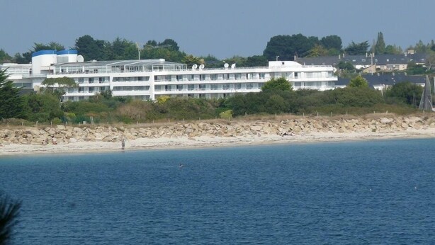 A multi-story hotel with a beach view, located near a rocky shoreline.