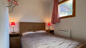 Un dormitorio con cabecera de madera, dos mesitas de noche con lámparas, una ventana con vistas a edificios y un radiador.