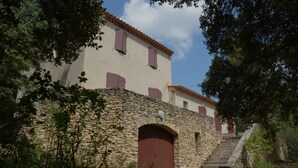 A stone building with a red door and windows, surrounded by greenery. - Villa sleeps 8 with superb pool   (La Tour-D'aigues)