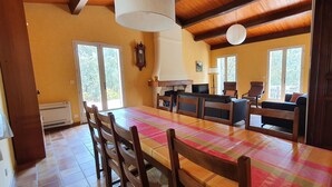 A dining area with a wooden table and chairs, a kitchen area with a stove and cabinets, and large windows with a view of greenery. - Villa sleeps 8 with superb pool   (La Tour-D'aigues)