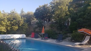 A swimming pool with lounge chairs and umbrellas, surrounded by trees and a stone wall. - Villa sleeps 8 with superb pool   (La Tour-D'aigues)