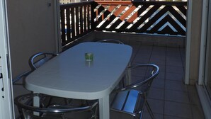 A balcony with a white table and chairs, a glass of drink, and a view of buildings and trees. - 54m² apartment rental with view of boats, shaded and sunny St Cyprien (Pyrénées-Orientales)