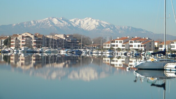 A marina with boats and buildings, a mountain range in the background, and clear skies. - 54m² apartment rental with view of boats, shaded and sunny St Cyprien (Pyrénées-Orientales)