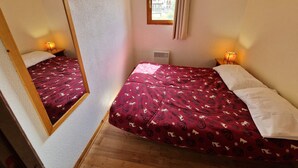 Une petite pièce agréable, avec un lit, une fenêtre avec des rideaux, un miroir et une petite table sur laquelle se trouve une lampe.