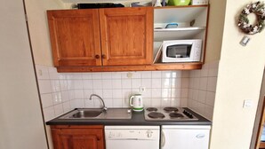 Une cuisine compacte dotée de meubles en bois, d’un évier, d’un four à micro-ondes, d’une bouilloire, d’un lave-vaisselle et d’un réfrigérateur.