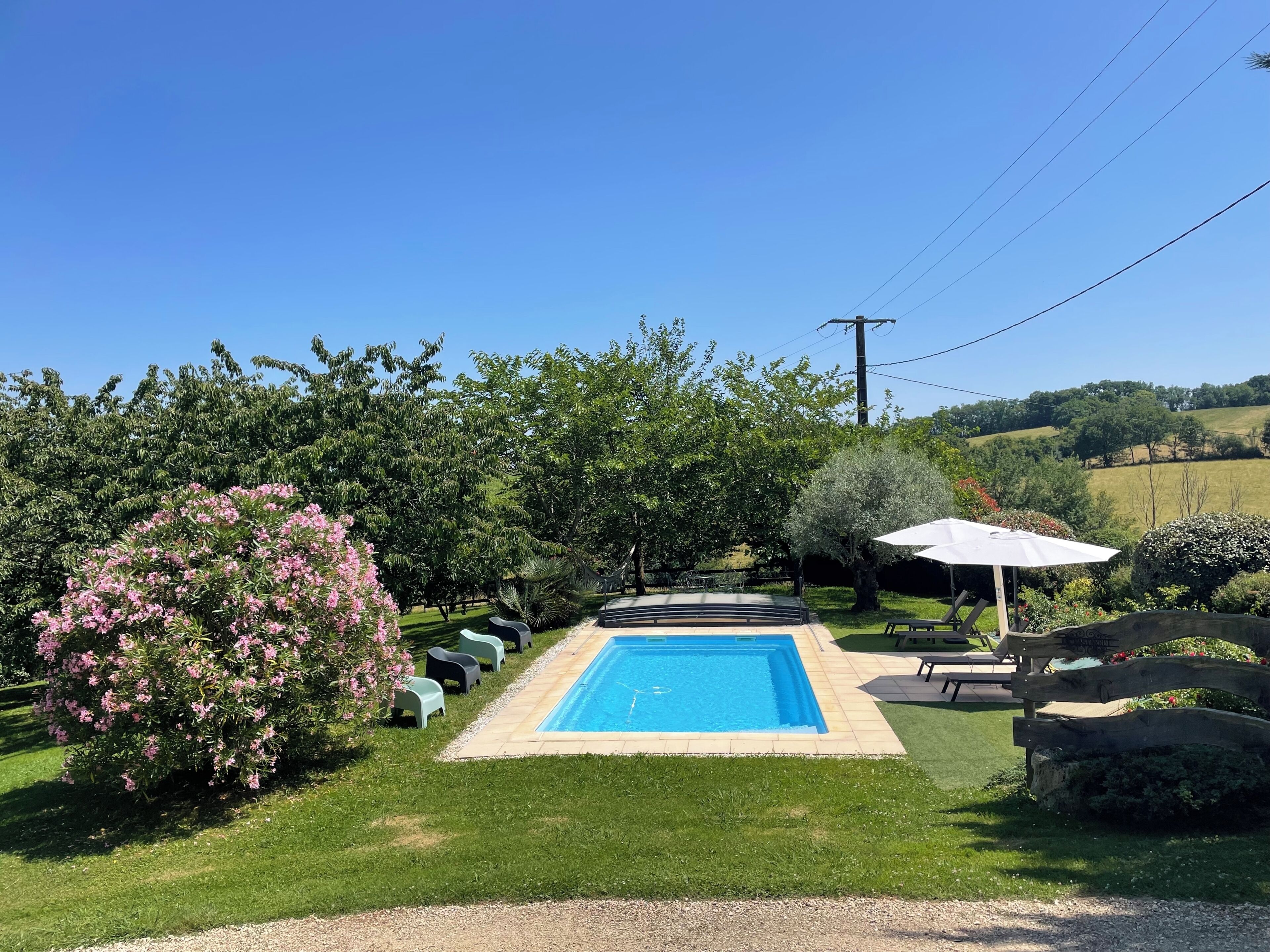Une piscine rectangulaire, bordée d’une terrasse carrelée, entourée d’une végétation luxuriante et surplombée d’un ciel bleu azur.