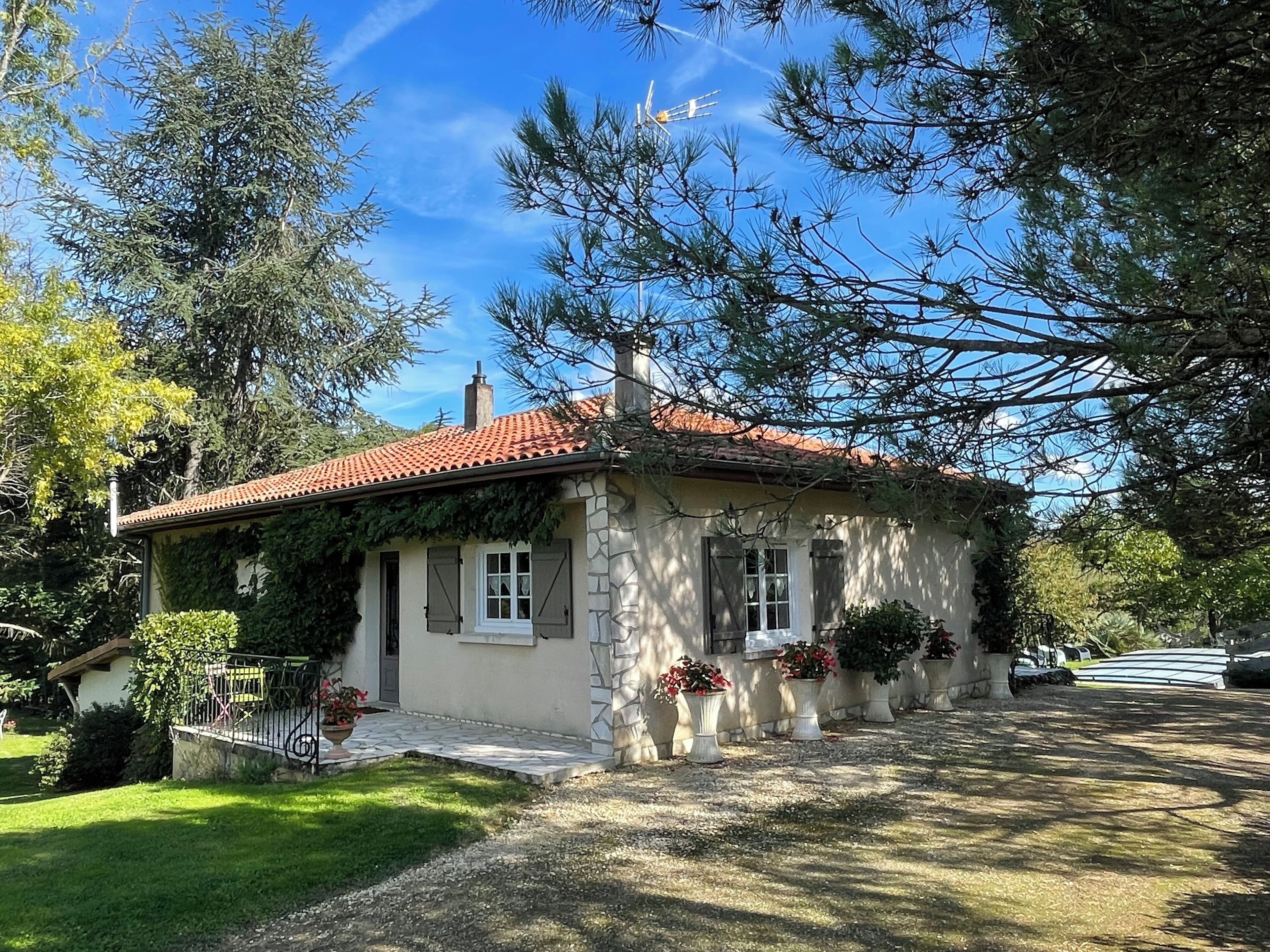 Una pequeña casa de piedra con techo de tejas rojas, rodeada de follaje y árboles.