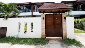 Un edificio moderno con entrada protegida, un porche cubierto y un pequeño jardín con una palmera.