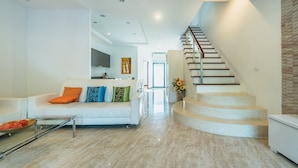 Una sala de estar moderna con un sofá blanco, una mesa de centro de vidrio y una escalera que sube a otro nivel.