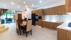Una cocina moderna con armarios de madera, un comedor con mesa y sillas, y vistas al exterior a través de grandes ventanales.