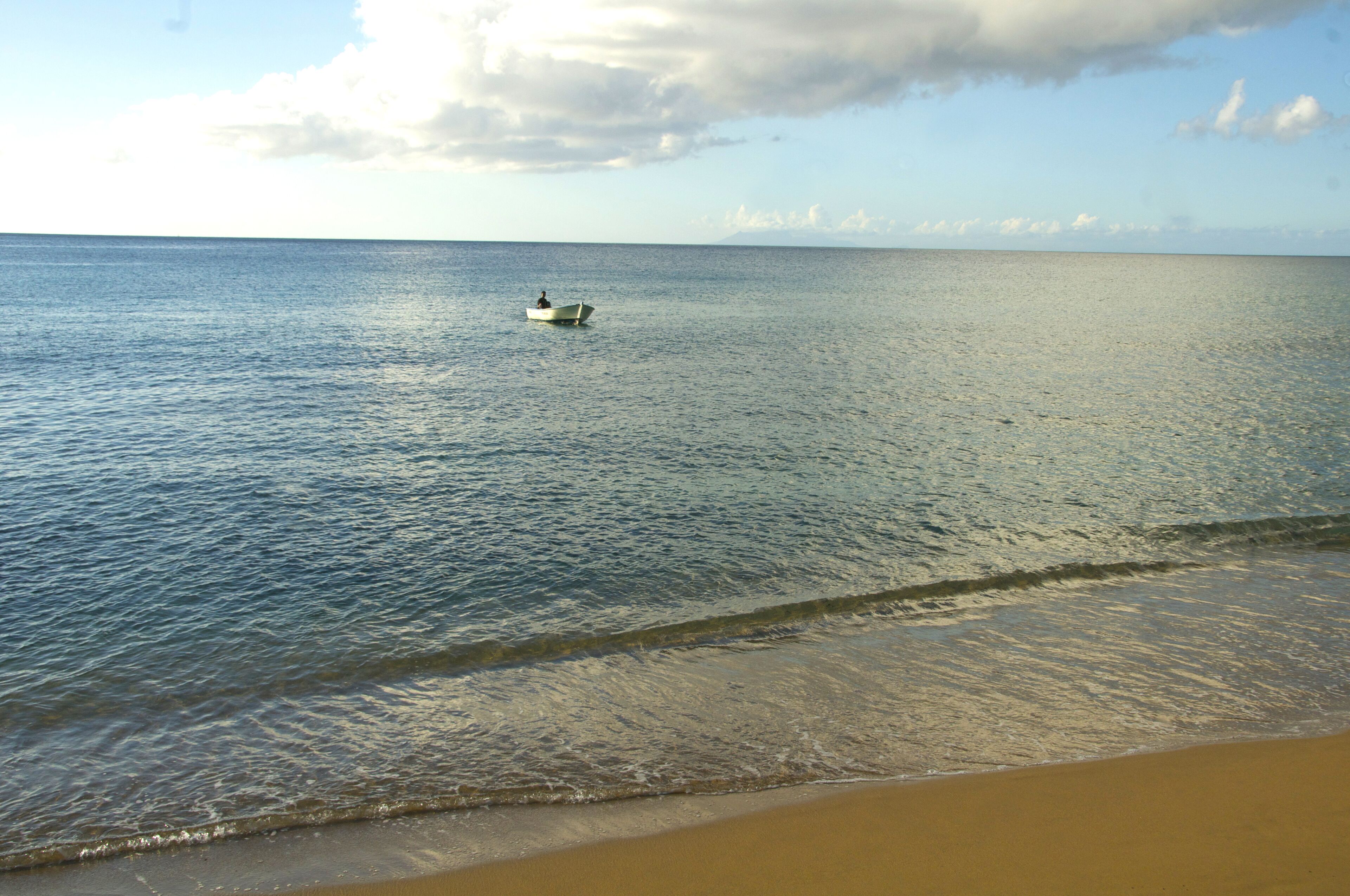 A calm sea with a boat in the distance and a sandy beach in the foreground.