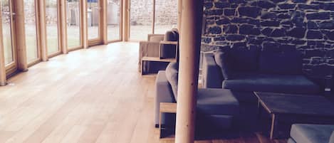 A spacious room with wooden flooring, a stone wall, and large windows.