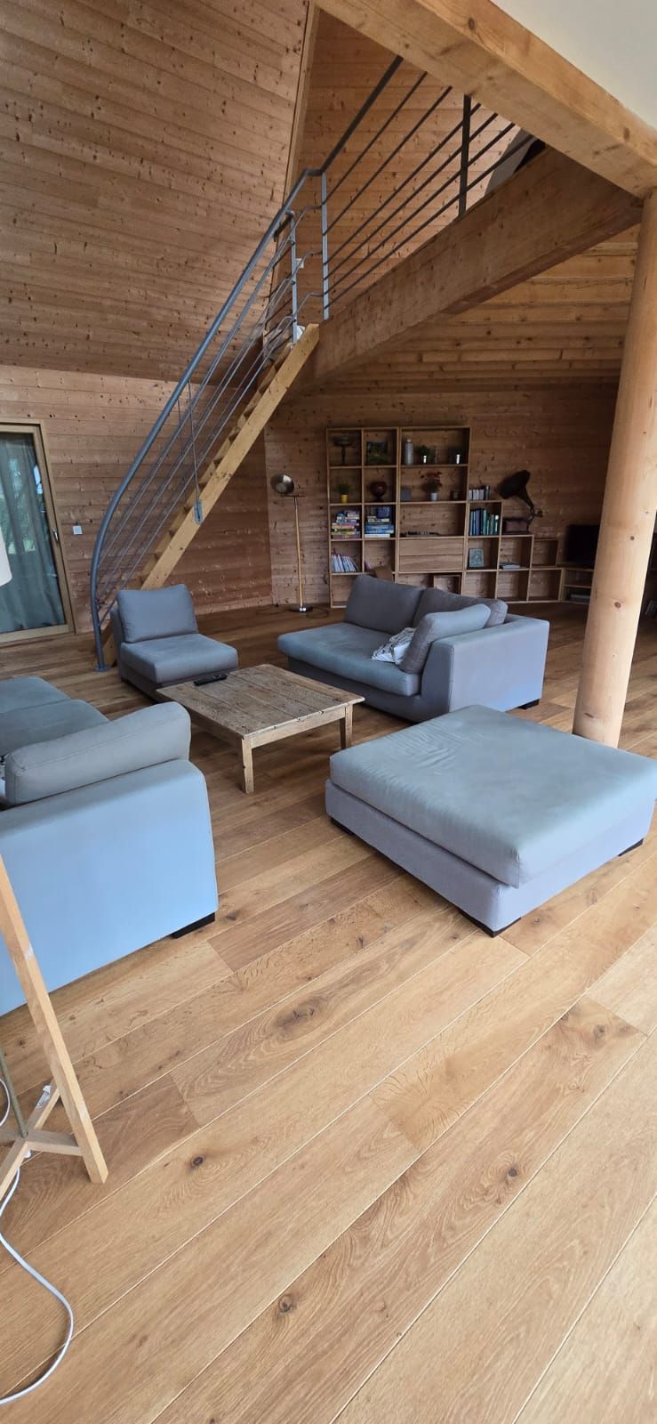 Un interior de madera con una escalera, sofás, una mesa de centro y una estantería.