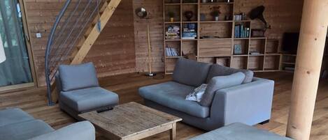 Un interior de madera con una escalera, sofás, una mesa de centro y una estantería.