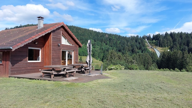Una cabaña de madera con techo rojo, una mesa de picnic y un banco.