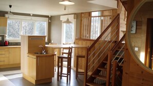 Una cocina con armarios de madera, una isla central y una escalera que sube a un nivel superior.