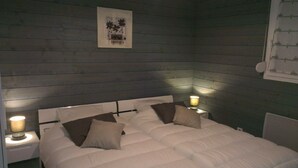 Una cama bien hecha con ropa de cama blanca y dos almohadas, flanqueada por mesitas de noche con lámparas, en una habitación con paredes de madera y un cuadro en la pared.