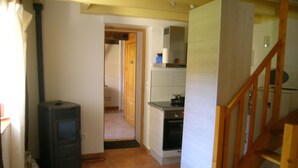 A narrow hallway with a wood-burning stove, a kitchen area with a stove and oven, and a staircase. - A country cottage "Ti Gwen" (Plonévez-Du-Faou)