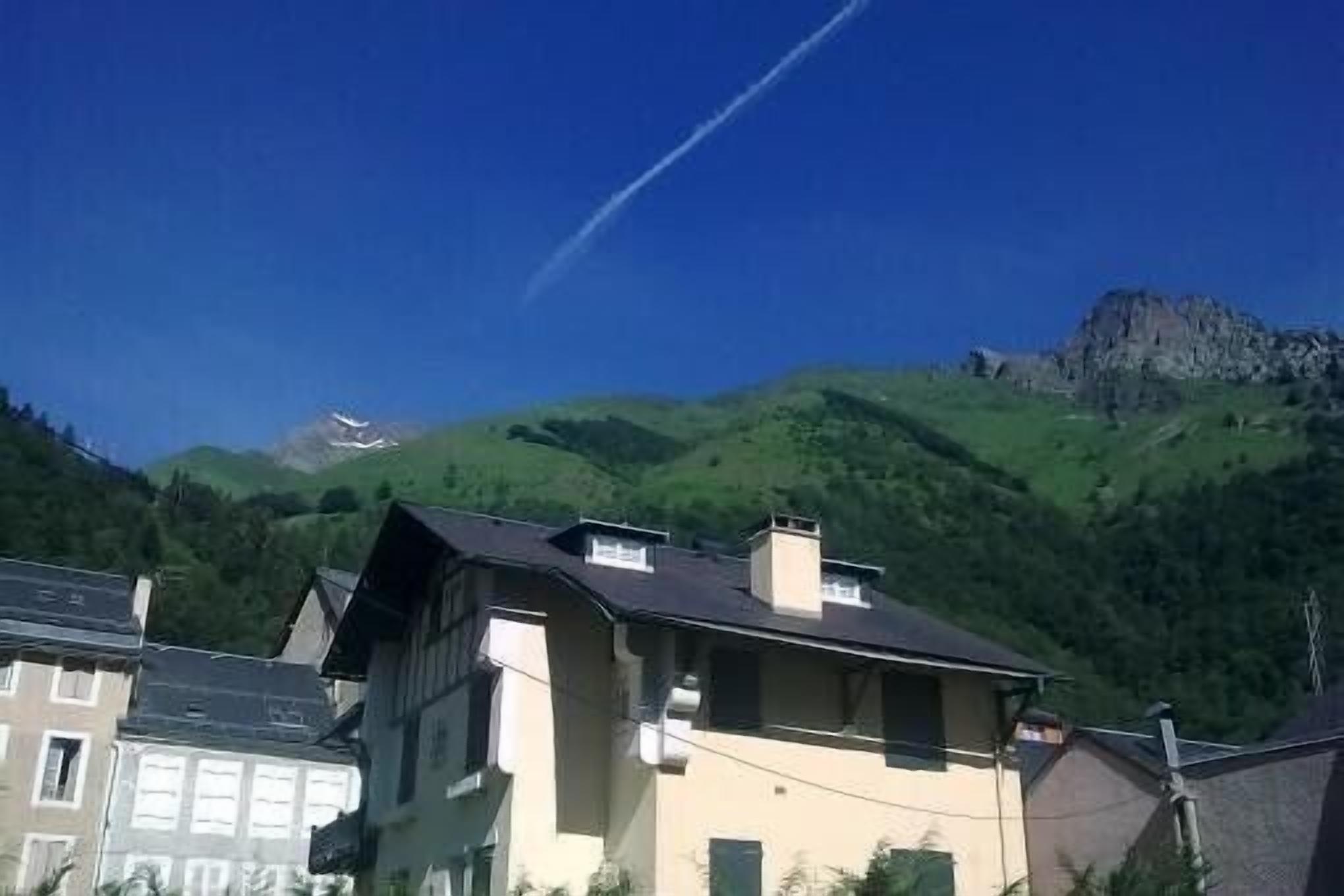A building with a sloped roof, surrounded by lush green hills and a clear blue sky.