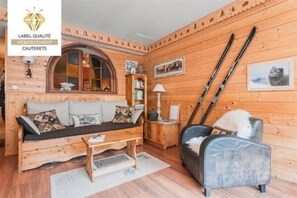 L’intérieur d’un chalet confortable, avec des murs en bois, un canapé en bois, un fauteuil et des paires de skis appuyés contre le mur.