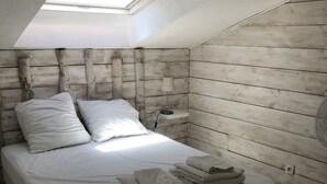 A bedroom with a skylight, a wooden headboard, a bed with white linens, a bedside table with a lamp, and a stack of towels.