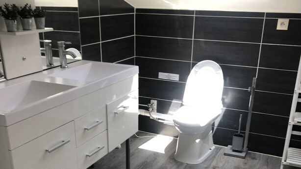 A modern bathroom with a white vanity, black tiled walls, and a wooden floor.