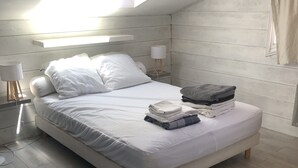 A modern bedroom with a skylight, a neatly made bed, a bedside lamp, and a stack of folded towels.