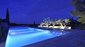 Ein Pool mit blau beleuchtetem Rand, umgeben von Liegestühlen und Bäumen.