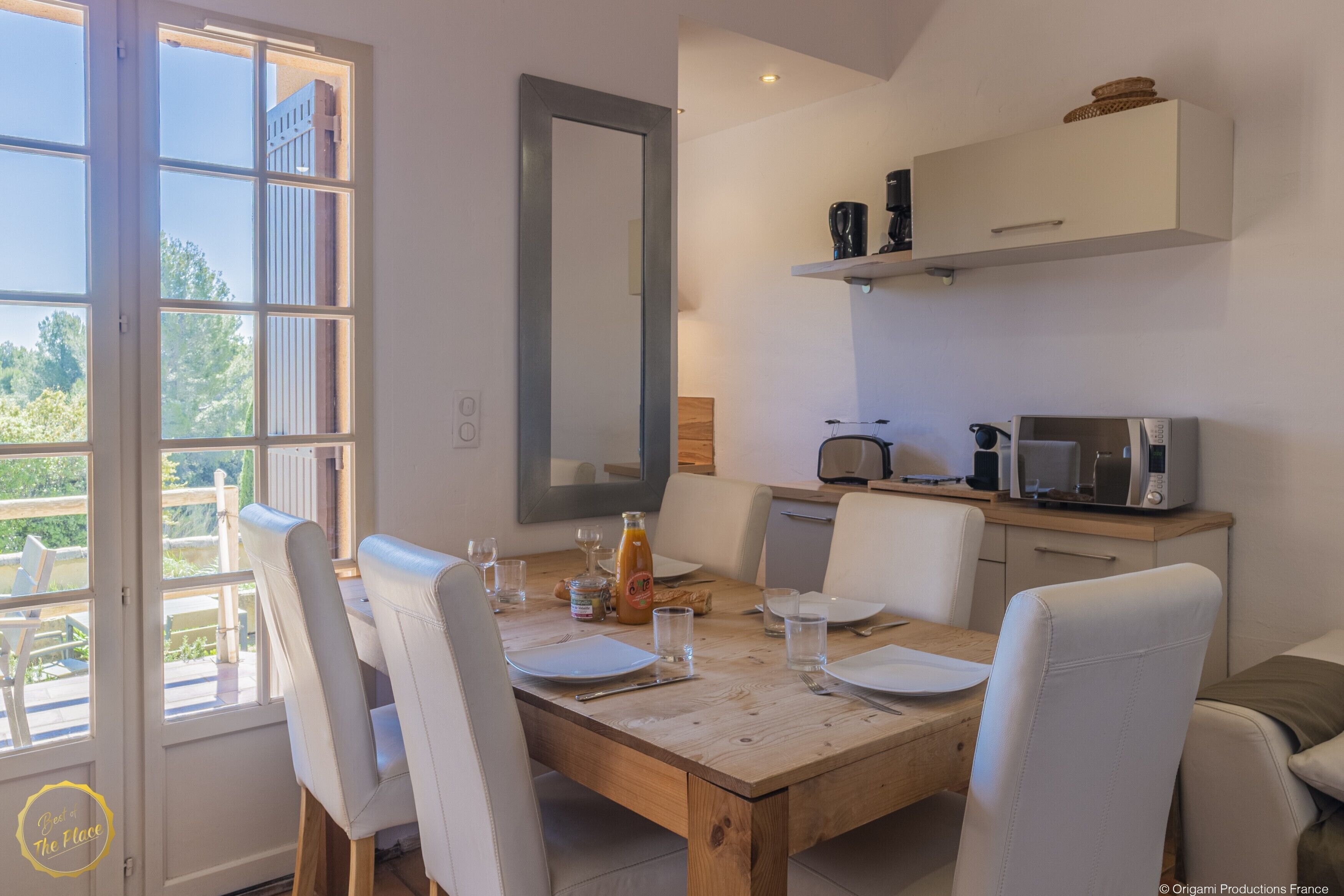A dining area with a wooden table, white chairs, and a view of the outdoors through a large window.