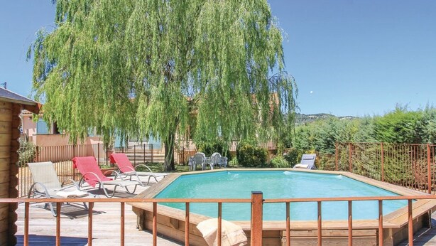Una terraza de madera con piscina, rodeada por una valla metálica.