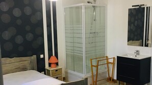 Un dormitorio con cama, mesita de noche, lámpara, ducha, espejo y cómoda.